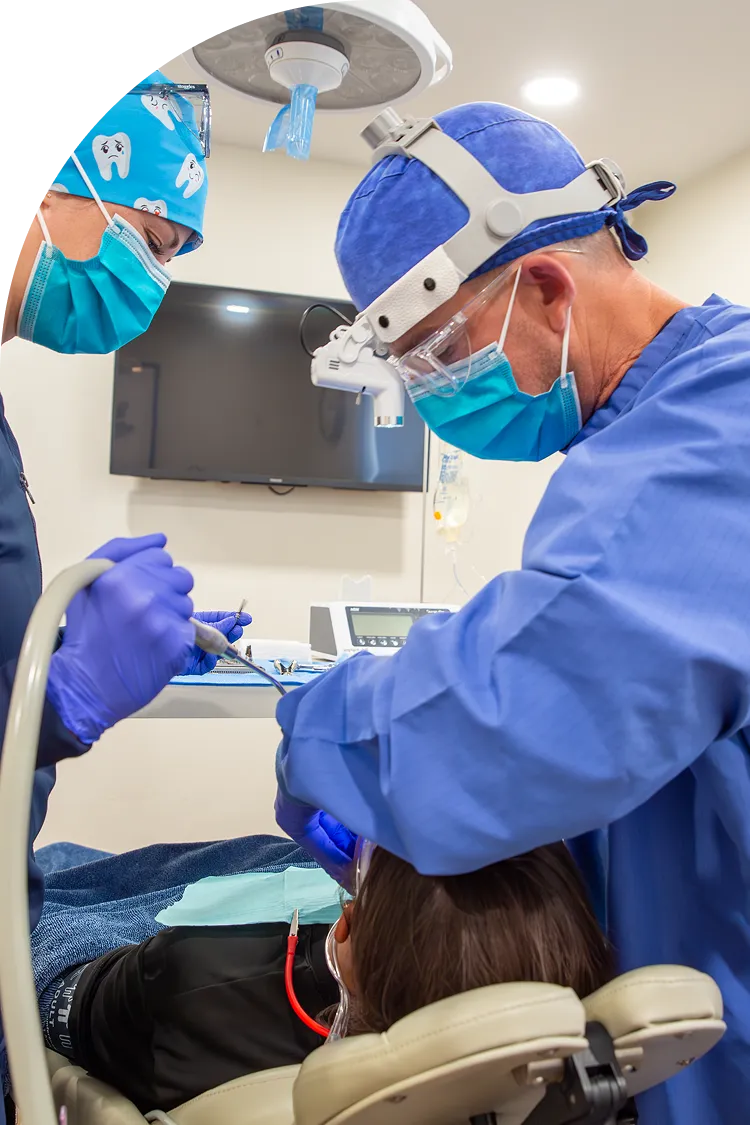 Oral surgeon and assistant treating a patient under the surgical light